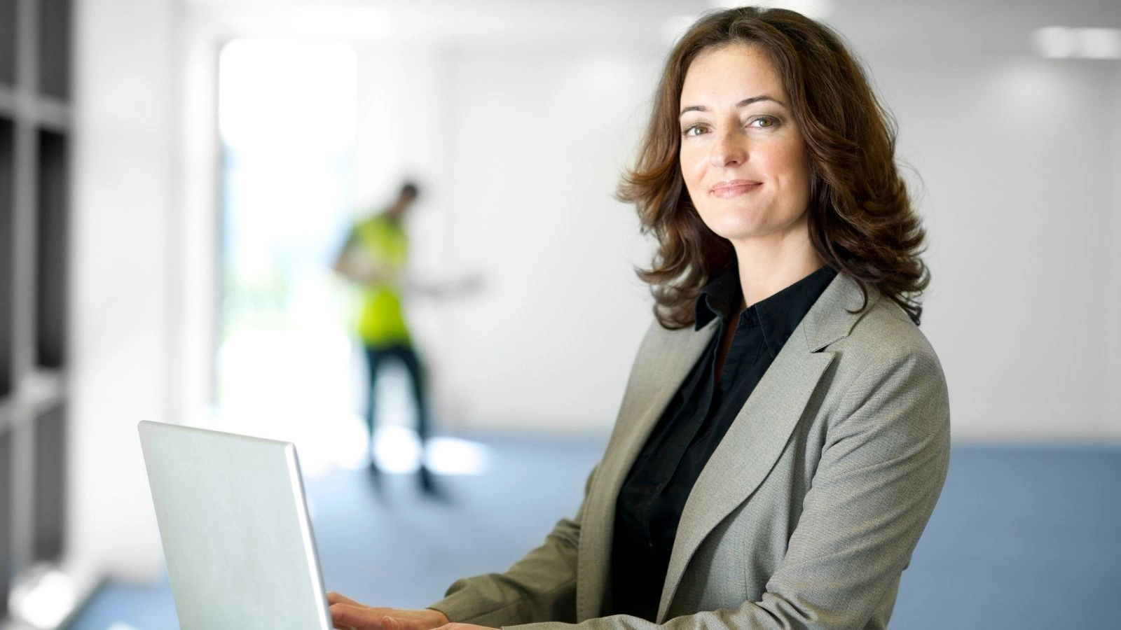 uśmiechnięta kobieta trzyma laptop, w tle prace remontowe